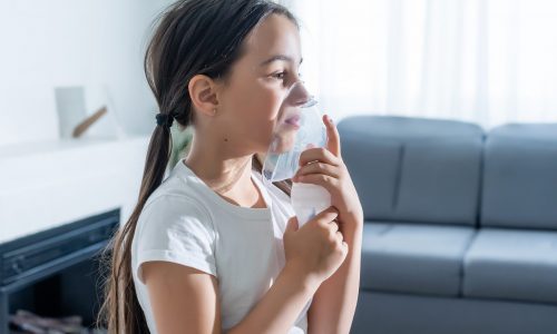 sick little girl makes inhalation over grey background with copy space. Girl making inhalation with nebulizer at home. child asthma inhaler inhalation nebulizer steam sick cough.